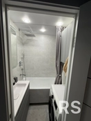 Выполнил комплексный ремонт ванной: уложена светлая керамическая плитка, установлены подвесная раковина, ванна с тропическим душем, стиральная машина и шкафчик, смонтированы точечные светильники.